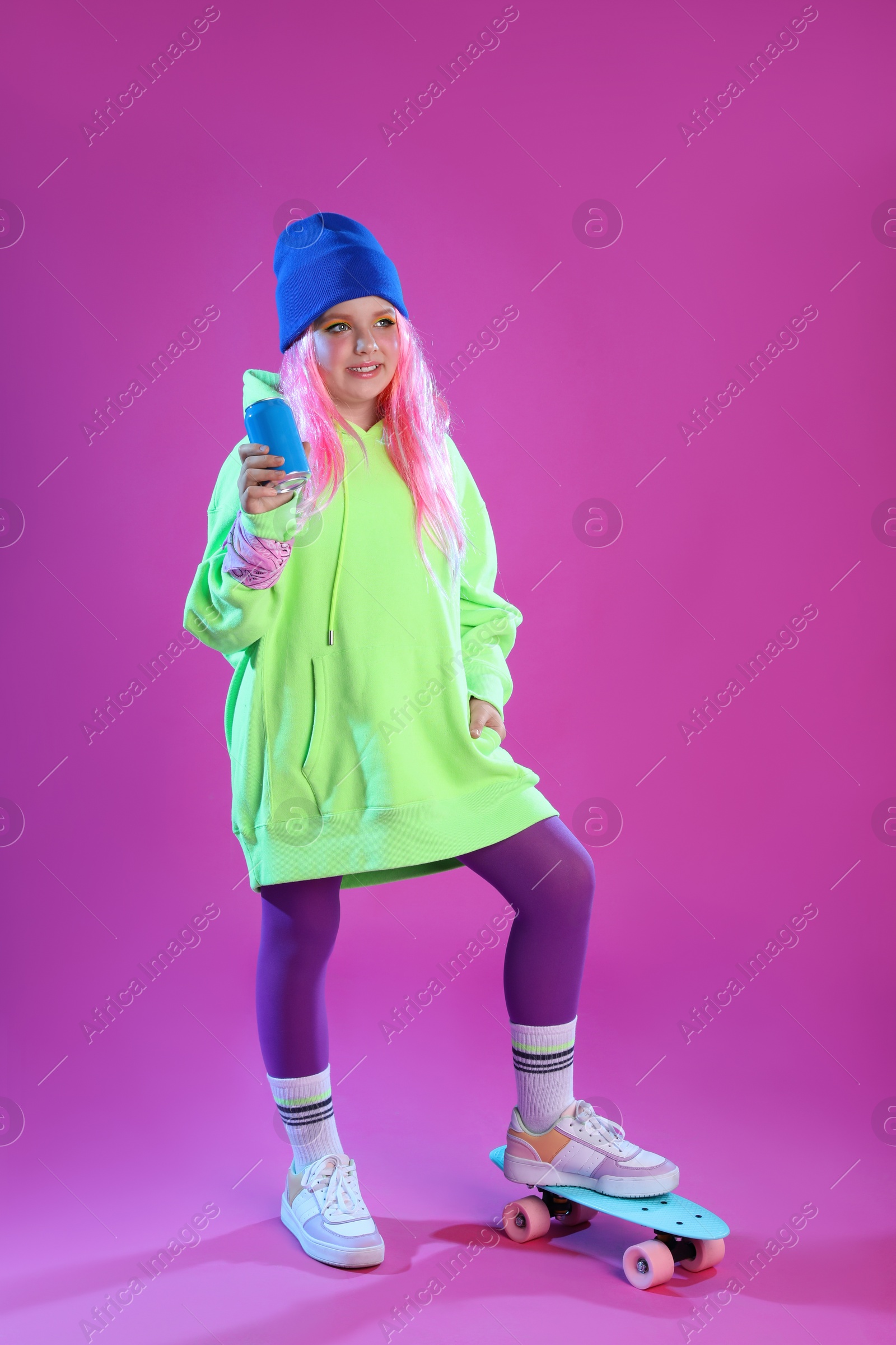 Photo of Cute indie girl with canned drink and penny board on violet background