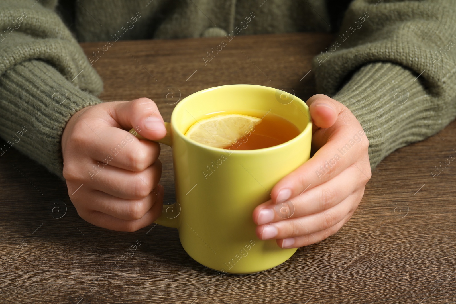 Photo of Woman holding mug of tea at wooden table, closeup