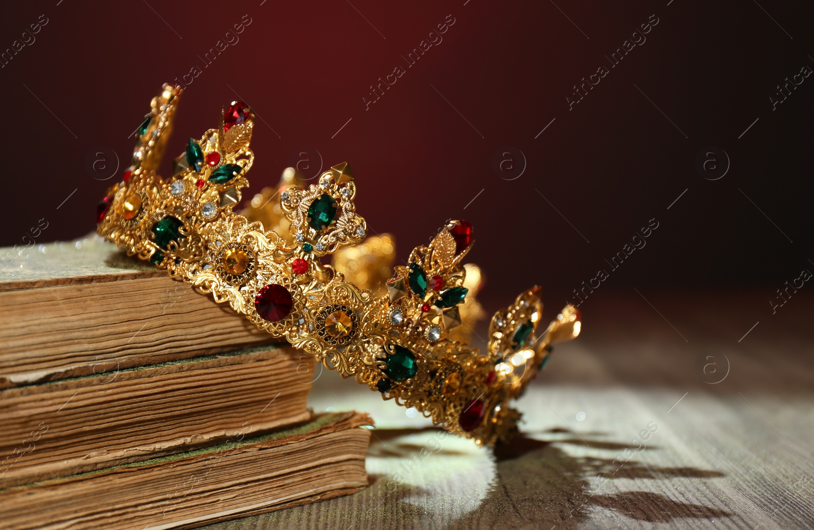 Photo of Beautiful golden crown and old books on wooden table. Fantasy item