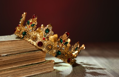 Beautiful golden crown and old books on wooden table. Fantasy item