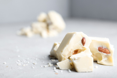Pieces of tasty white chocolate with nuts on light grey table, closeup. Space for text
