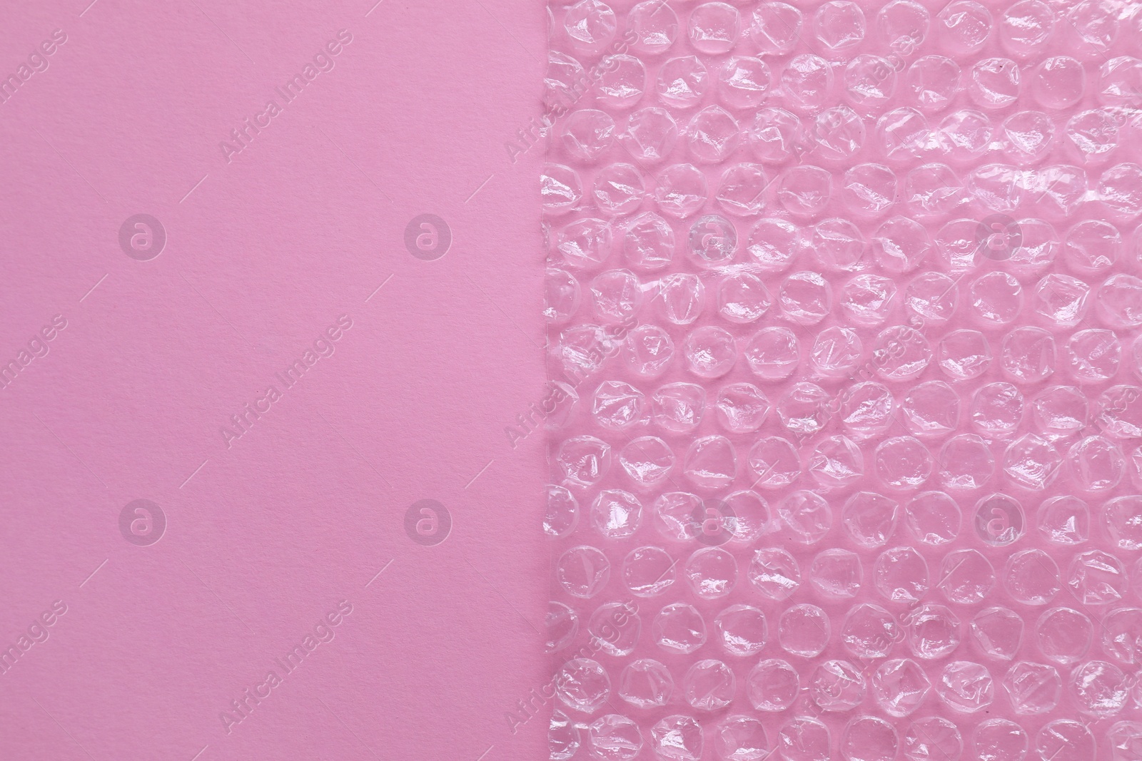 Photo of Transparent bubble wrap on pink background, top view. Space for text