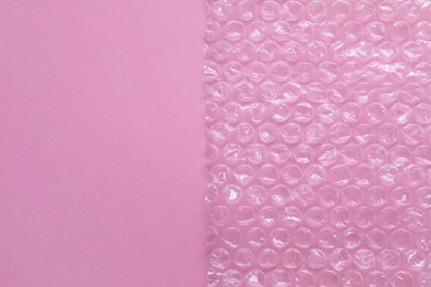 Photo of Transparent bubble wrap on pink background, top view. Space for text