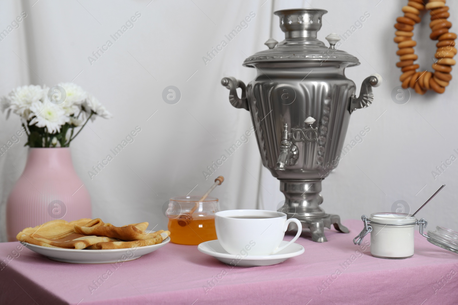 Photo of Vintage samovar, cup of hot drink and snacks served on table indoors. Traditional Russian tea ceremony