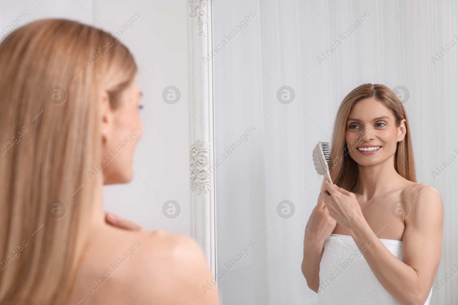 Photo of Beautiful woman brushing her hair near mirror in room