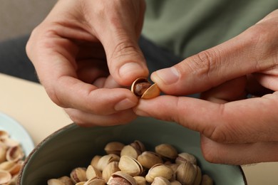 Photo of Woman opening tasty roasted pistachio nut at table, closeup