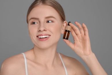 Beautiful young woman with bottle of essential oil on light grey background