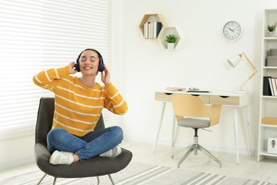 Photo of Happy woman in headphones enjoying music on cosy armchair at home