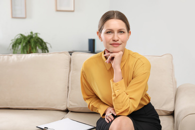 Photo of Professional psychotherapist with clipboard on sofa in office