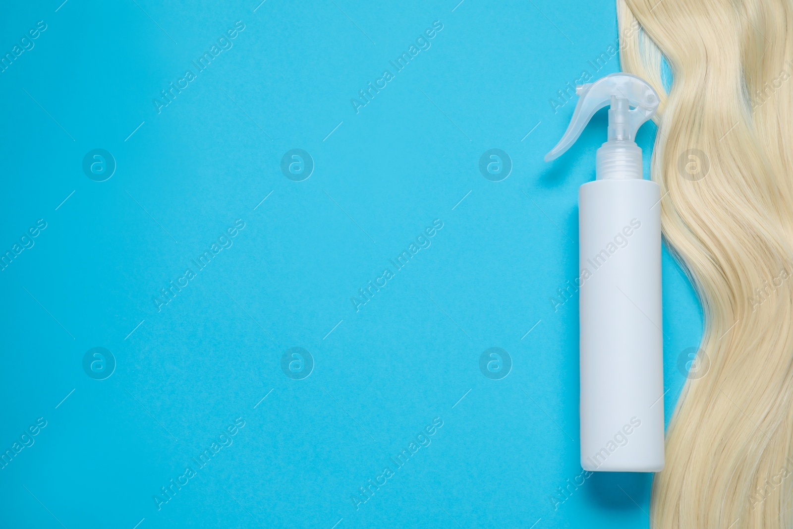 Photo of Spray bottle with thermal protection and lock of blonde hair on light blue background, flat lay. Space for text