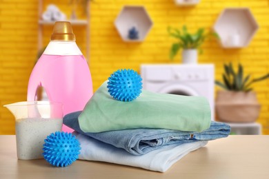 Image of Dryer balls, detergents and stacked clean clothes on wooden table in laundry room