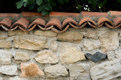 Photo of Old stone wall with red roof tiles outdoors
