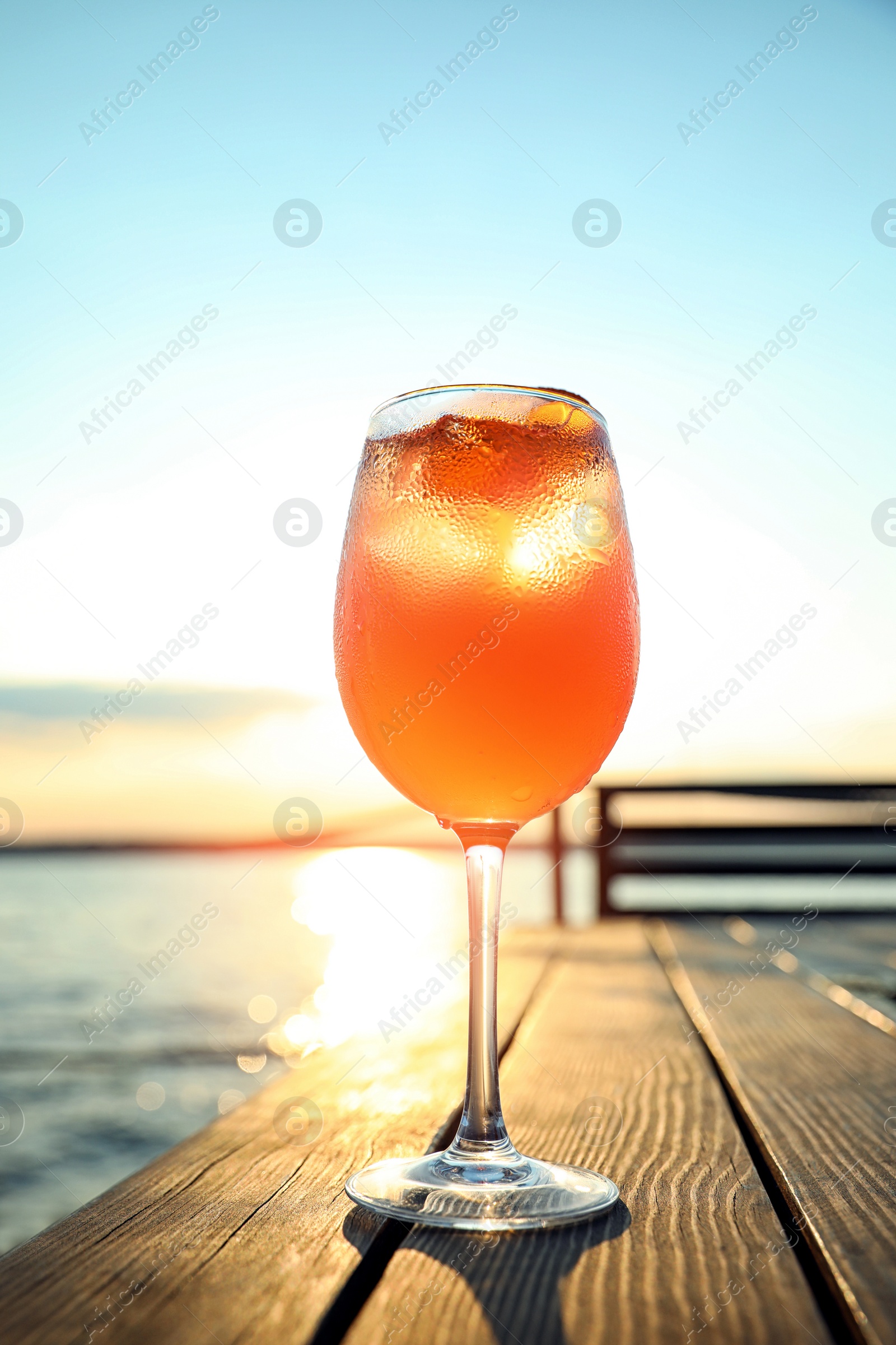 Photo of Glass of fresh summer cocktail on wooden table outdoors at sunset