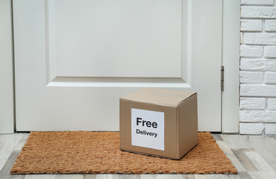 Photo of Parcel with sticker Free Delivery on rug indoors. Courier service