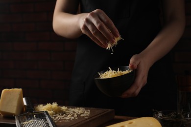 Woman with grated cheese at wooden table, closeup