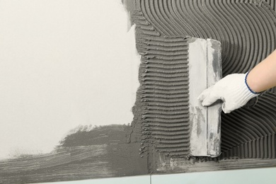 Closeup of worker spreading concrete on wall with spatula, space for text. Tile installation