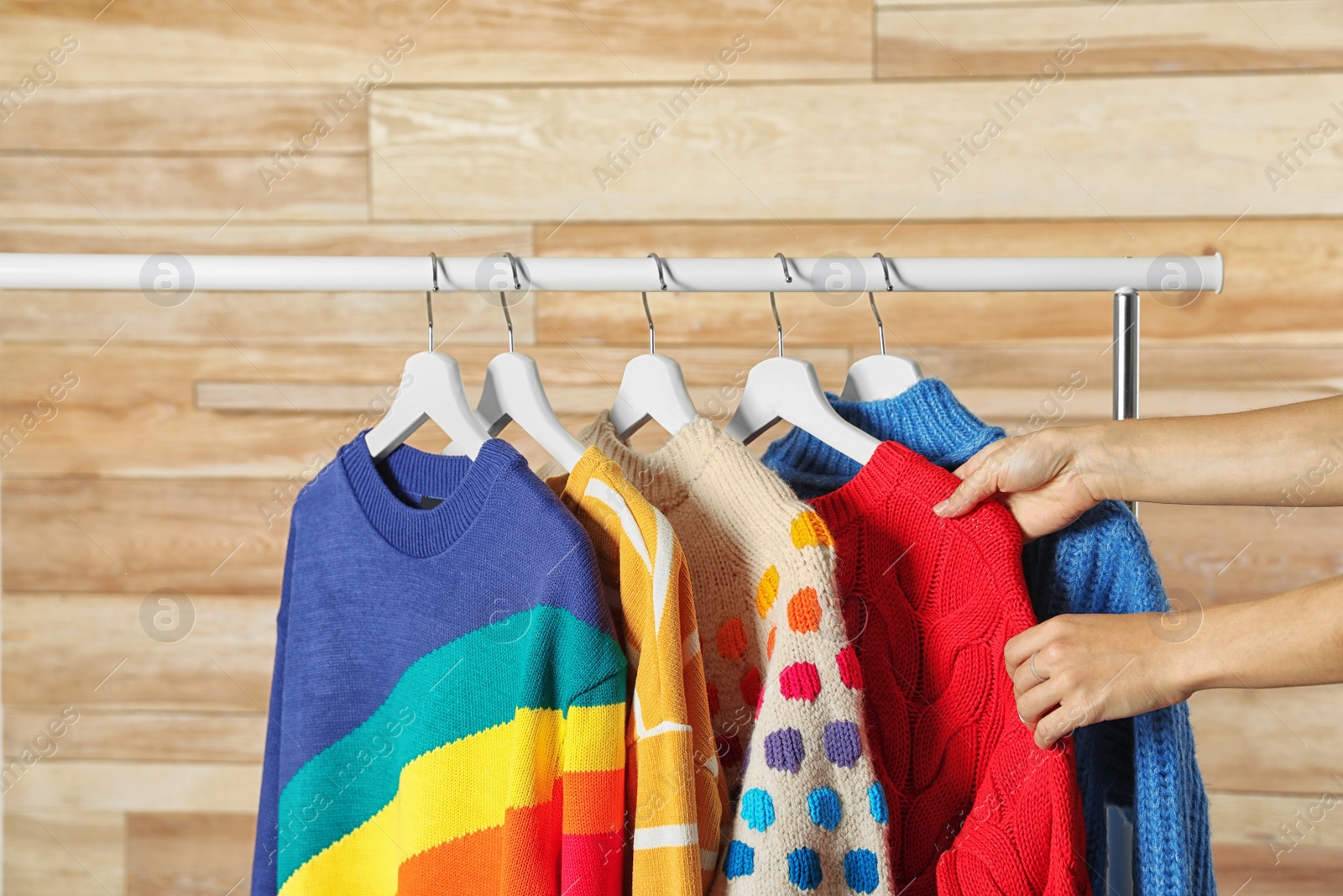 Photo of Woman choosing sweater on rack against wooden background