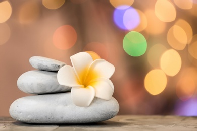 Photo of Stack of spa stones and flower on table against blurred lights. Space for text