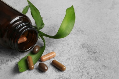 Photo of Bottle with vitamin capsules and green leaves on table, space for text