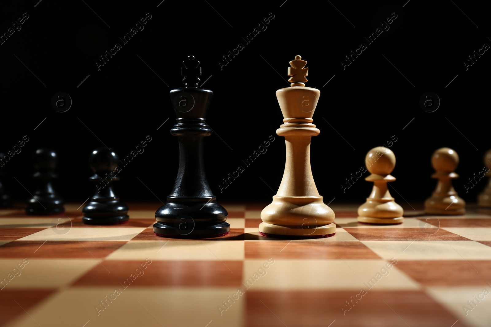 Photo of Kings with pawns on wooden chess board against black background