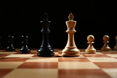 Photo of Kings with pawns on wooden chess board against black background