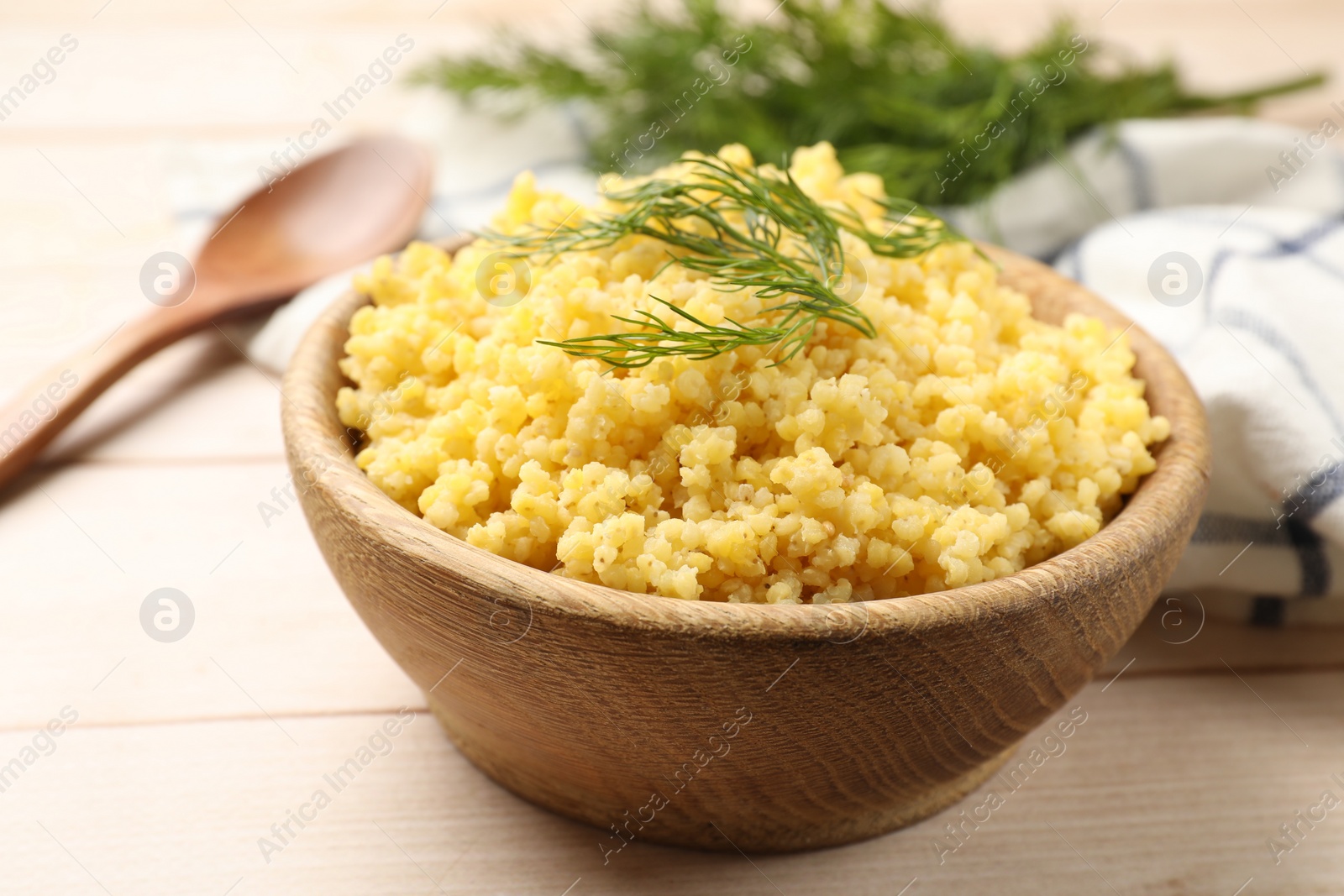 Photo of Tasty millet porridge and dill in bowl on light wooden table, closeup