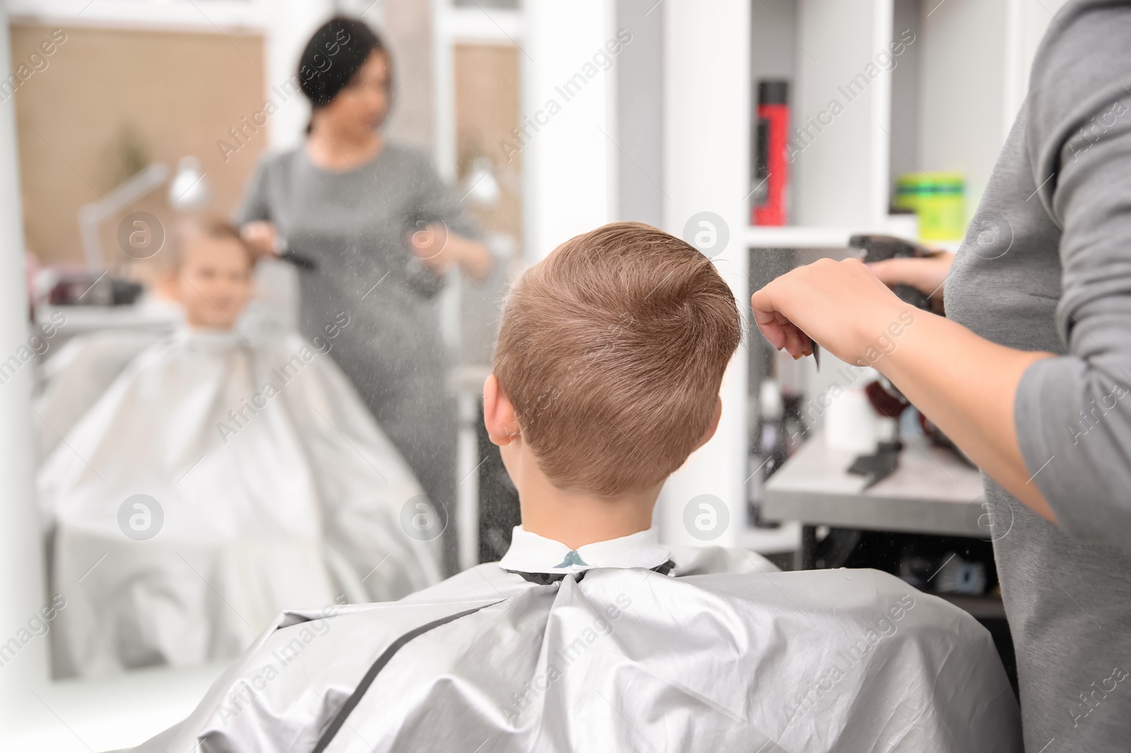 Photo of Professional female hairdresser working with little boy in salon