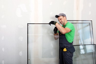 Photo of Worker in uniform preparing double glazing window for installation indoors