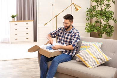 Photo of Young man opening parcel on sofa at home