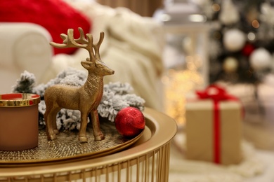 Photo of Christmas composition with decorative reindeer on golden table in room, closeup. Space for text