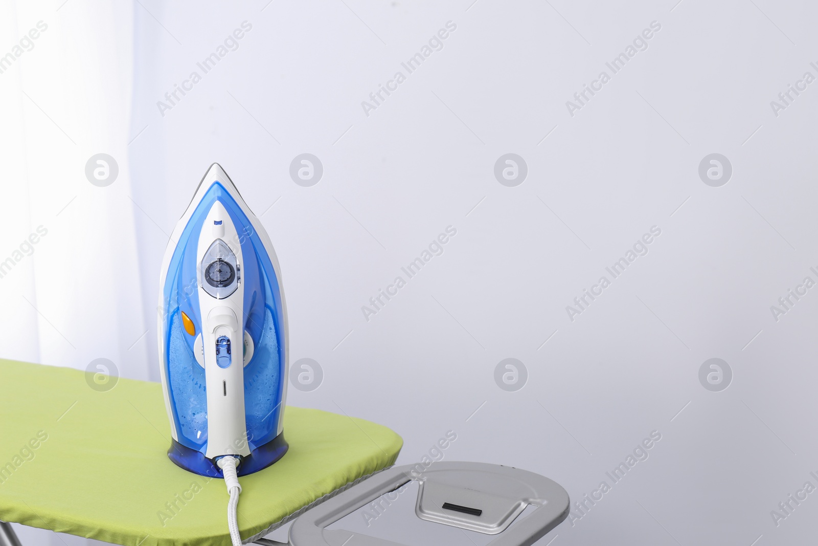 Photo of Modern electric iron on board indoors, space for text