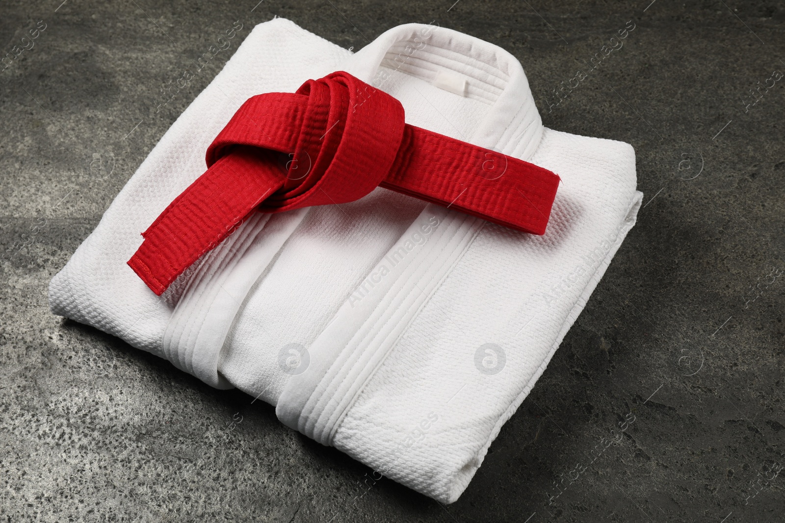 Photo of Red karate belt and white kimono on gray textured background