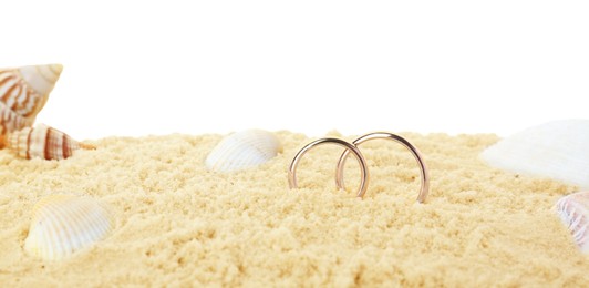 Photo of Honeymoon concept. Two golden rings, seashells and sand isolated on white