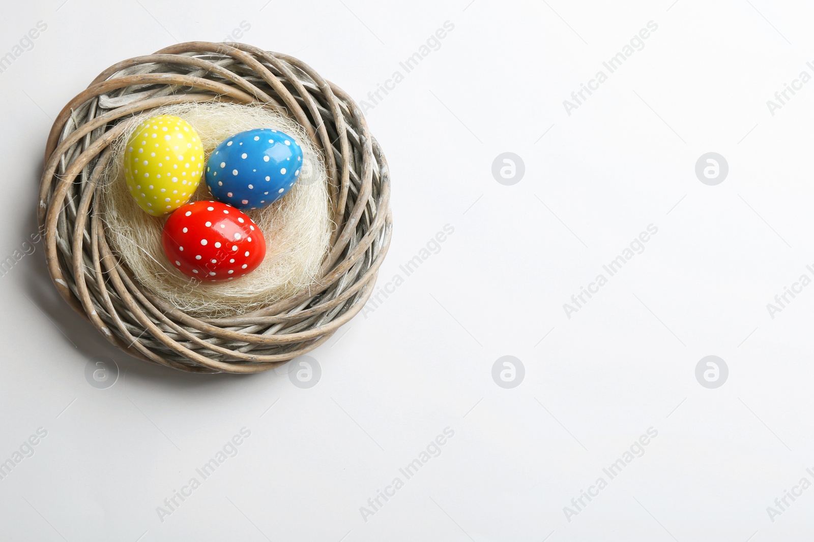 Photo of Wicker nest with painted Easter eggs on white background, top view