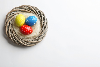 Wicker nest with painted Easter eggs on white background, top view