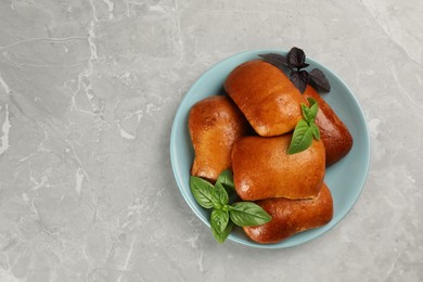 Photo of Delicious baked pirozhki and basil on light grey marble table, top view. Space for text