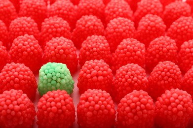 Delicious green gummy raspberry candy among red ones on pink background