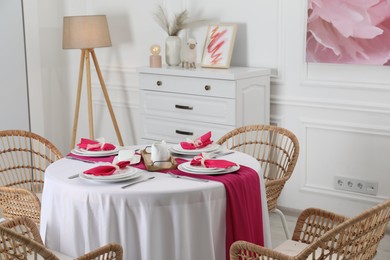 Photo of Color accent table setting. Plates, cutlery and pink napkins in dining room