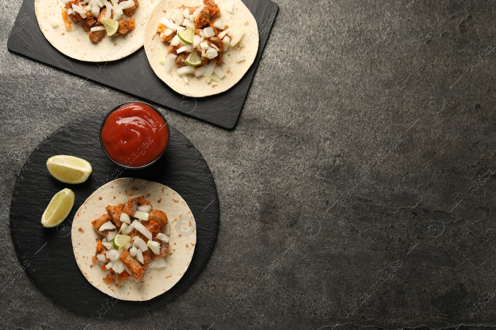 Photo of Delicious tacos with vegetables, meat and ketchup on grey textured table, flat lay. Space for text