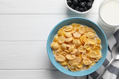 Photo of Bowl of tasty corn flakes and blueberries served on white wooden table, flat lay. Space for text