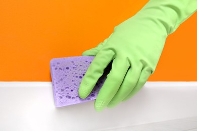 Woman in protective glove cleaning plinth with sponge indoors, closeup