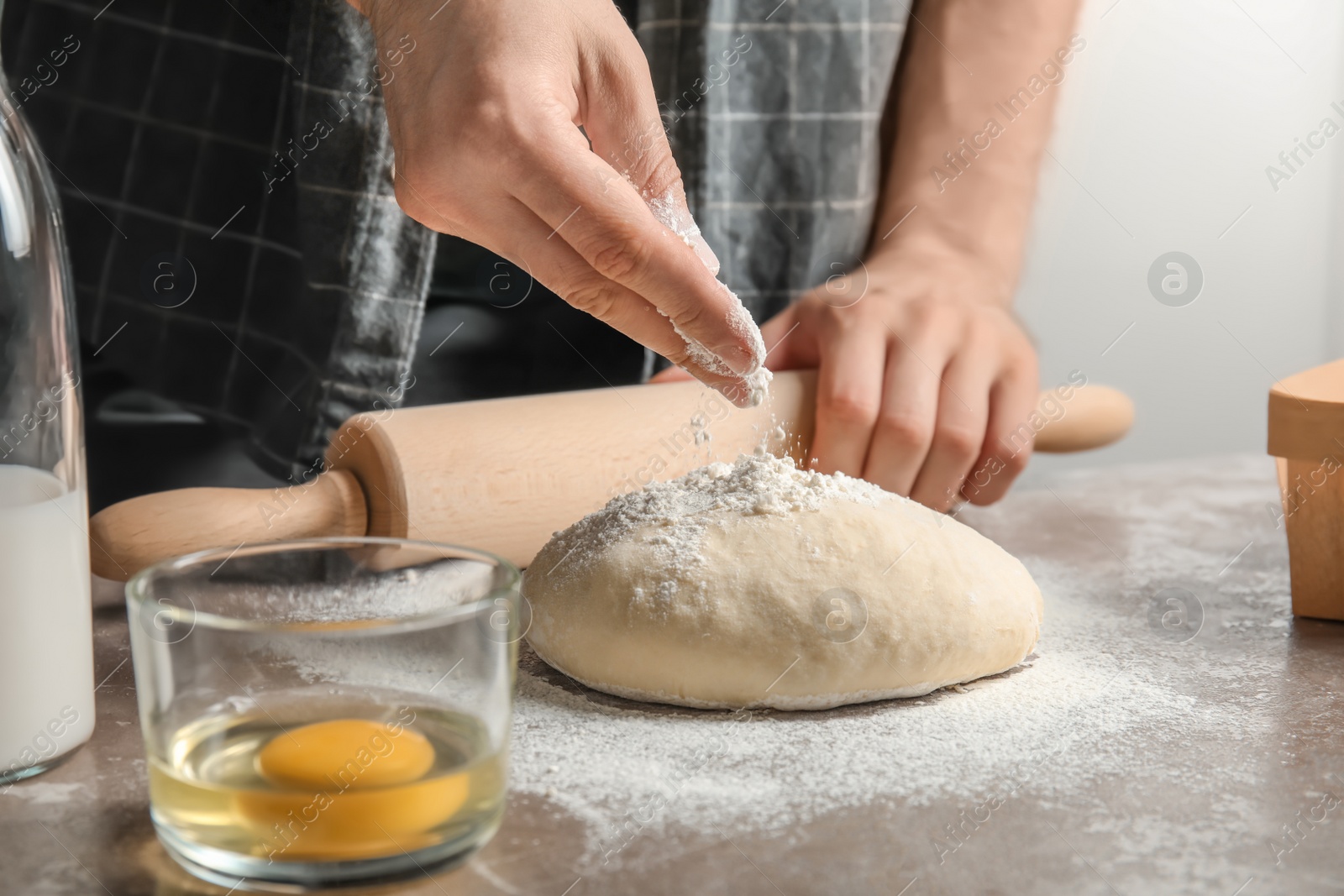 Photo of Man sprinkling dough for pastry with flour on table