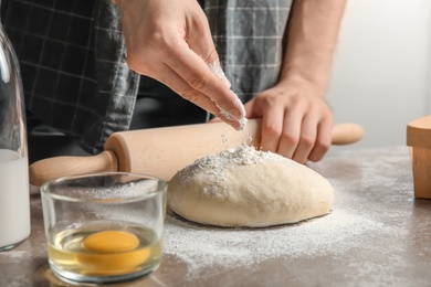 Man sprinkling dough for pastry with flour on table