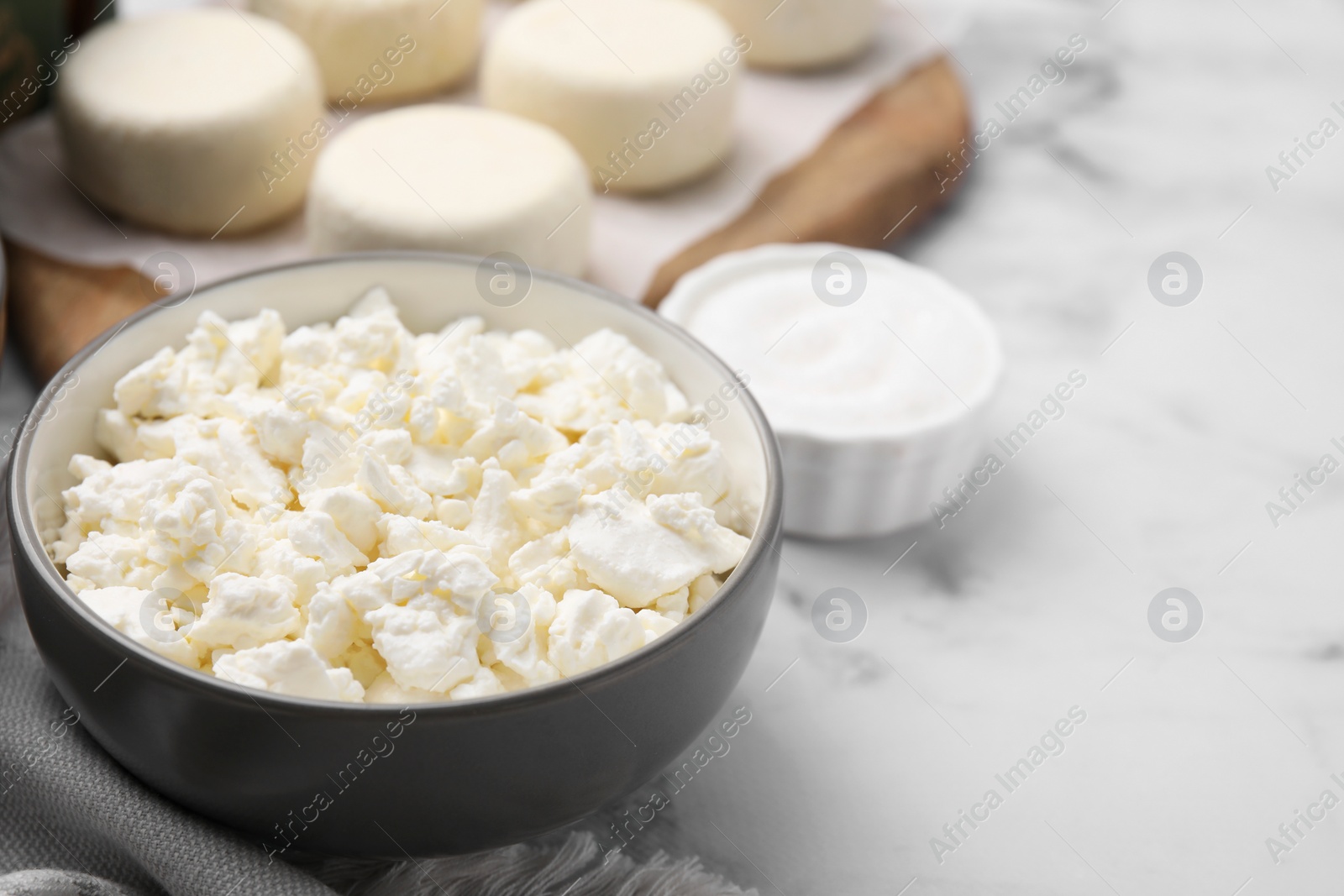 Photo of Bowl with dairy ingredient for cooking cottage cheese pancakes on white marble table, closeup and space for text