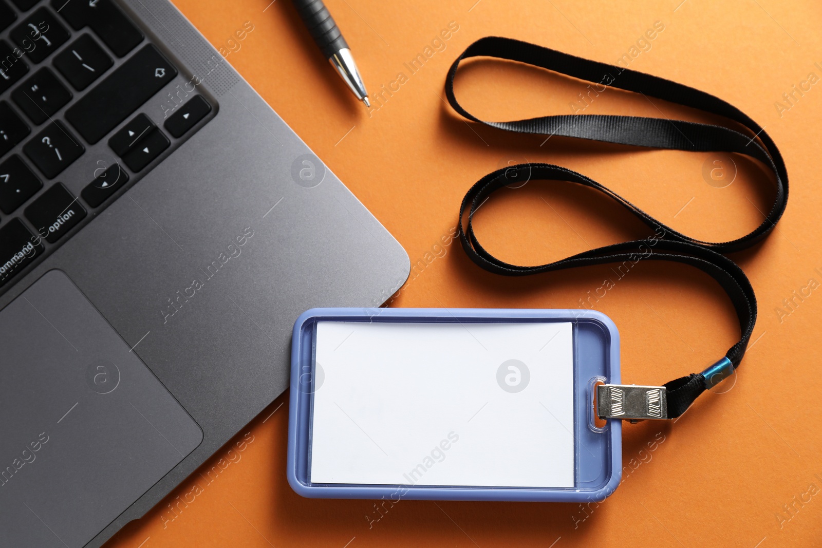 Photo of Blank badge, pen and laptop on orange background, top view