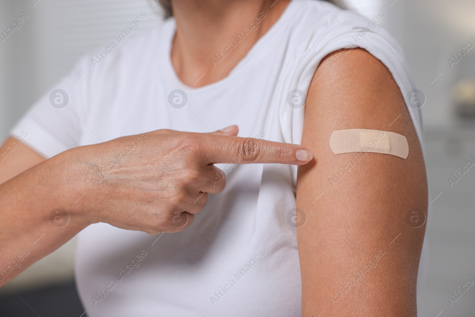 Photo of Woman pointing at adhesive bandage after vaccination against blurred background, closeup