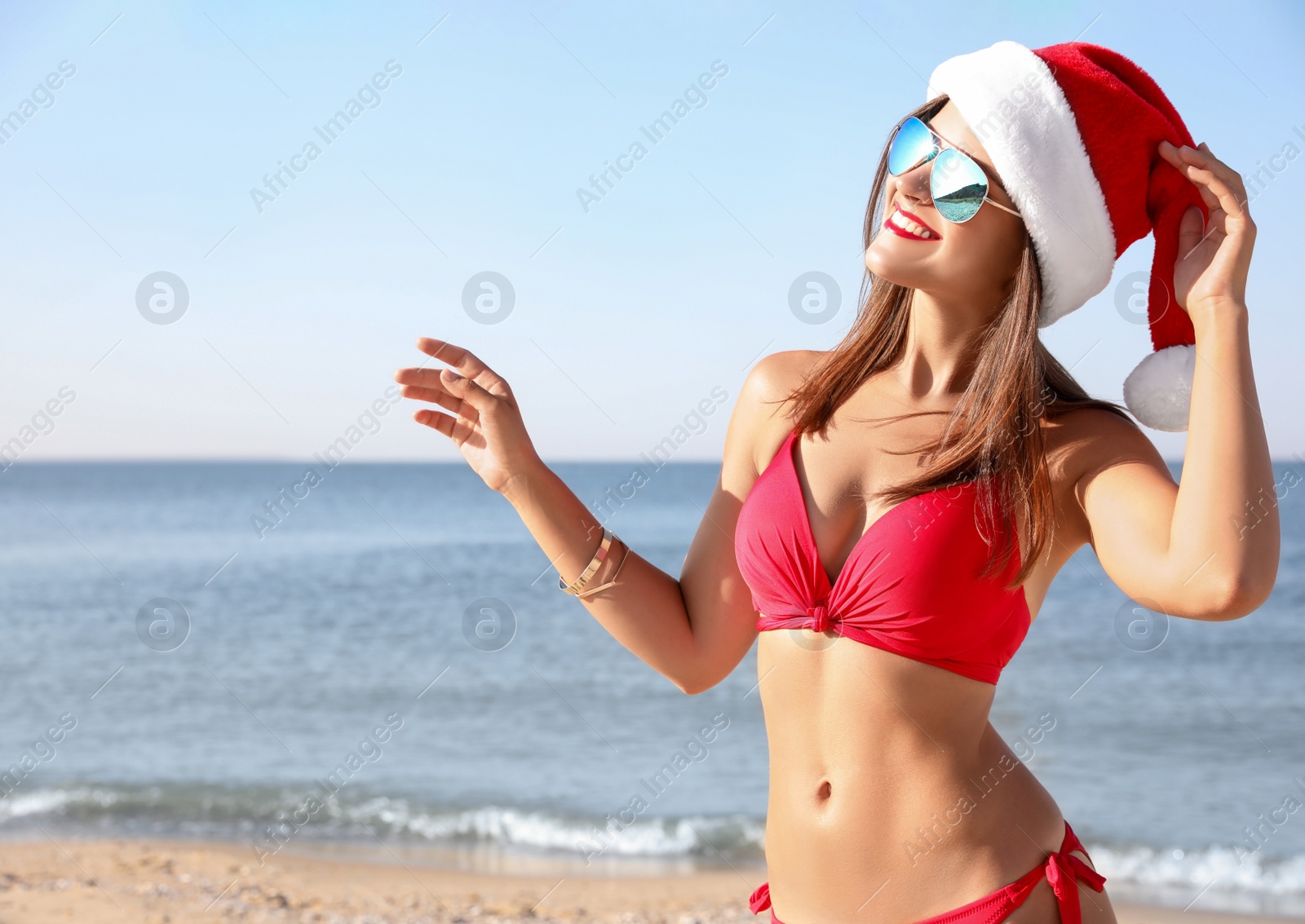 Photo of Young woman wearing Santa hat and bikini on beach. Christmas vacation