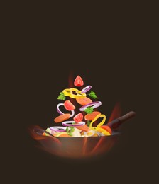 Image of Wok with tasty ingredients and fire on dark background