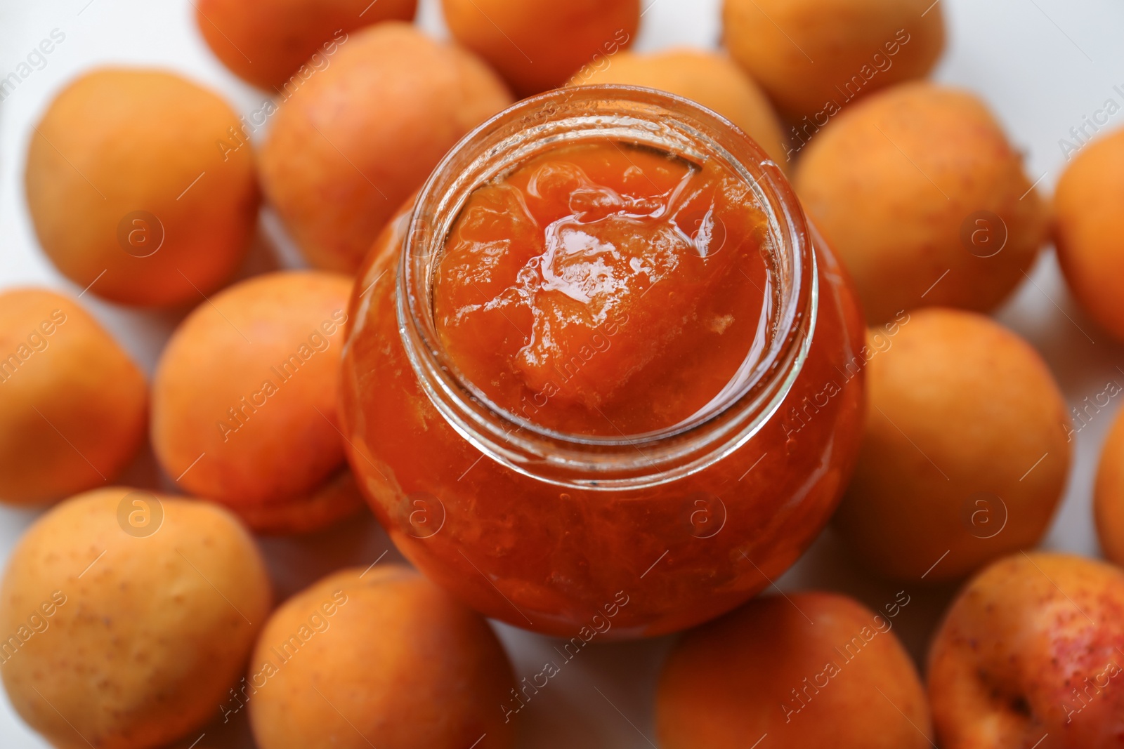 Photo of Jar of delicious jam and fresh ripe apricots on white background. Fruit preserve