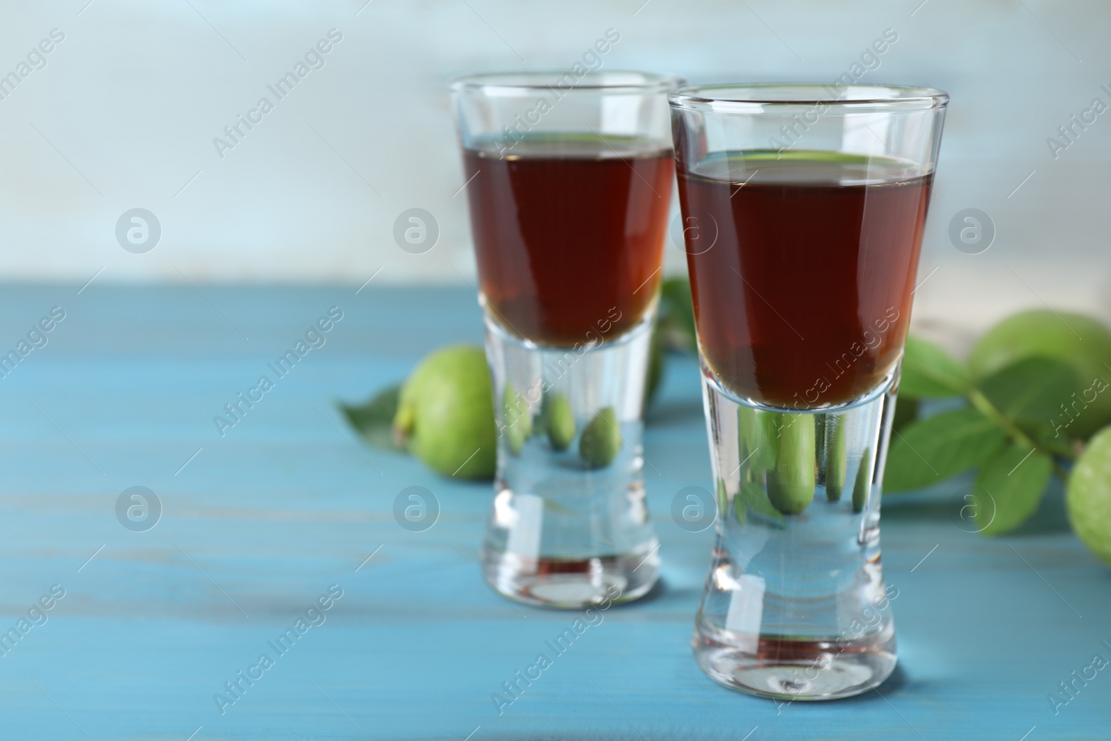 Photo of Delicious liqueur and green walnuts on light blue wooden table, closeup. Space for text